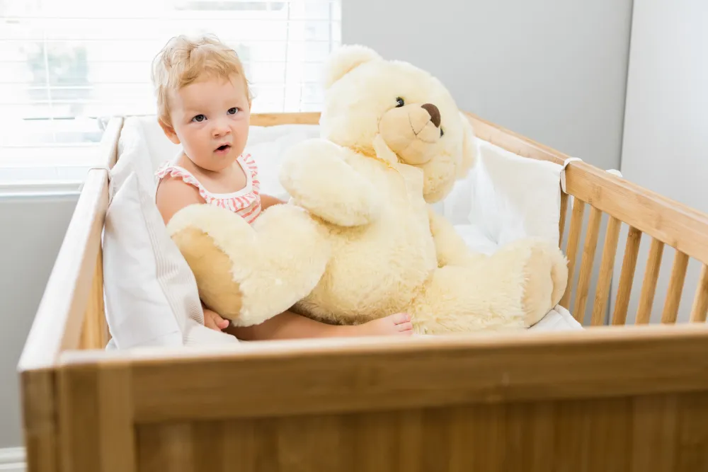 Baby spielt in der Wiege mit einem Teddybären