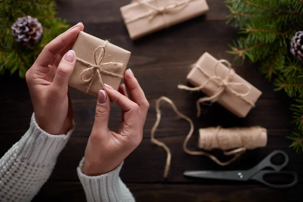 Hände binden eine Kordel um in Packpapier verpackte Geschenke