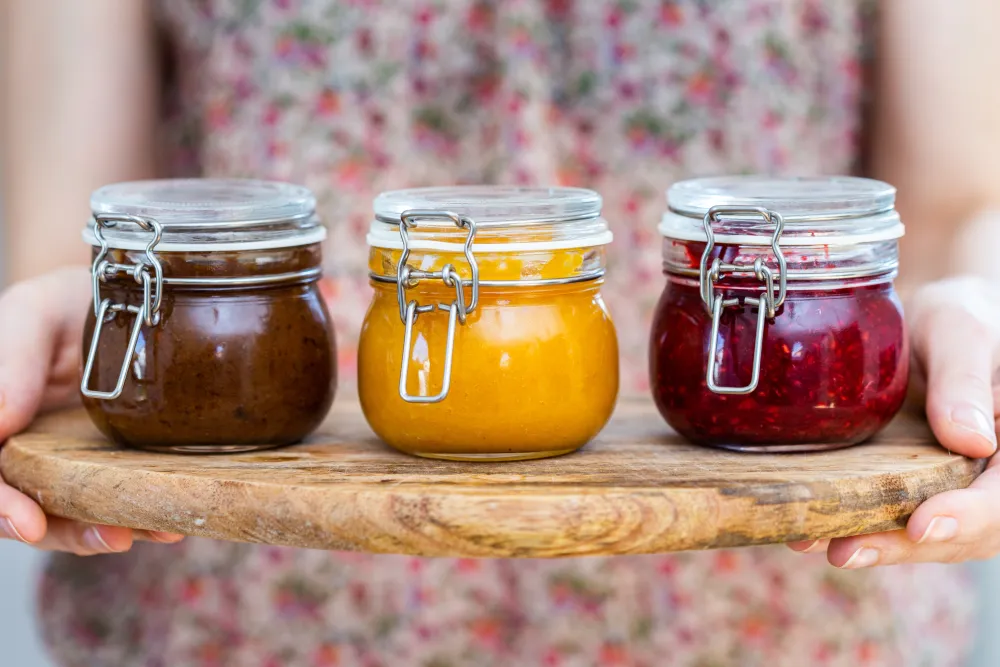 Frau hält ein Holzbrett mit Gläsern selbstgemachter Marmelade